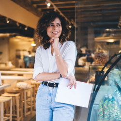 年轻的女企业家站在咖啡馆外，手里拿着文件，面带微笑